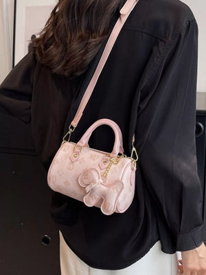 Pink mini barrel crossbody bag with all-over monogram pattern and elephant charm detail.