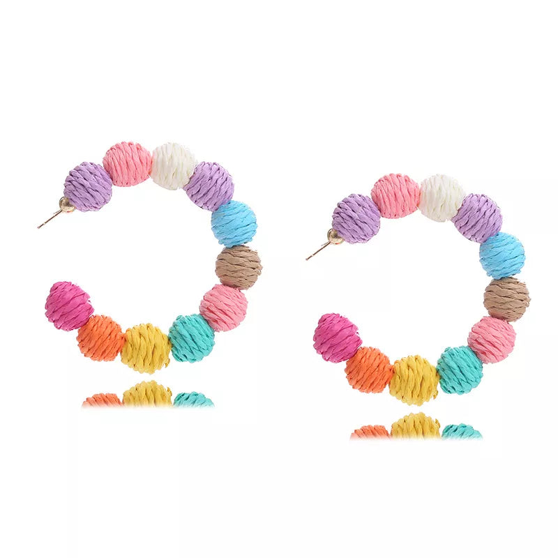 Raffia grass C-hoop earrings with colorful pom-pom beads in pink, purple, white, blue, brown, and yellow.