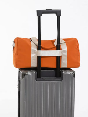 Orange duffle bag with beige straps and a detachable pouch on a grey suitcase.