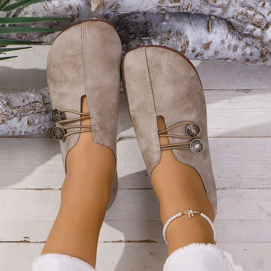 Tan leather slip-on flats with button detail and elastic lacing.