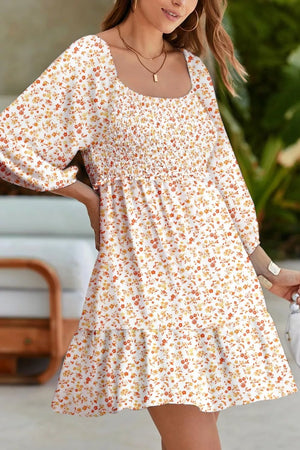 Floral smocked mini dress with square neckline and tiered skirt in beige with orange and yellow floral print.