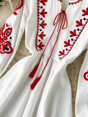 White maxi dress with red and blue embroidery, balloon sleeves, and tassel tie detail.