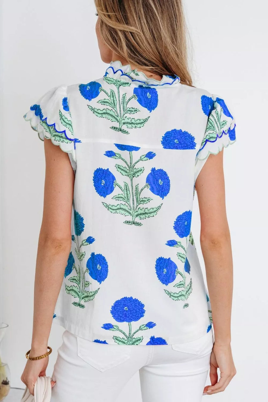 White cotton blouse with blue floral print, short flutter sleeves, and scalloped trim.