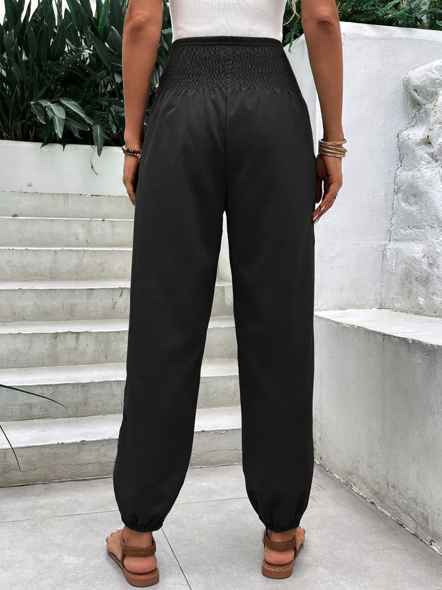 Black relaxed-fit trousers with smocked waistline and cuffed ankles.