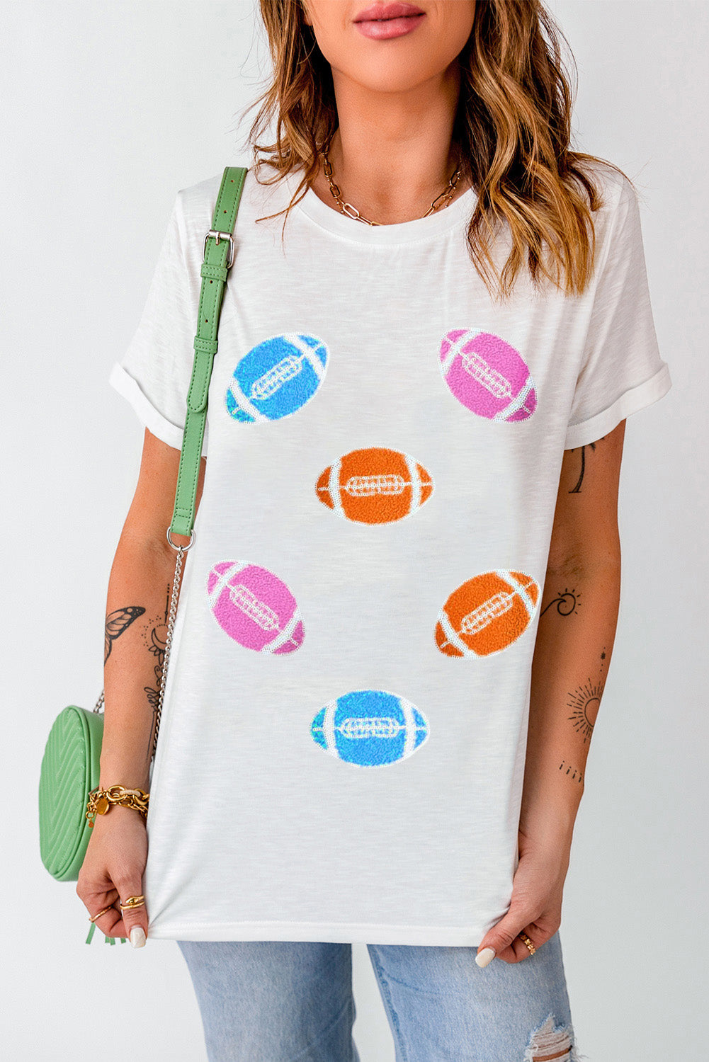 White t-shirt with rolled sleeves and scattered colorful football graphics.