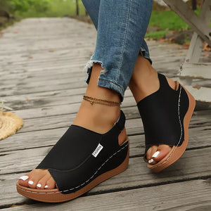 Black open-toe wedge sandals with white stitching detail and a brown sole.