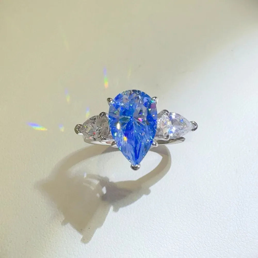 Silver trilogy ring with a bright blue pear cut moissanite center stone and two smaller pear cut stones.