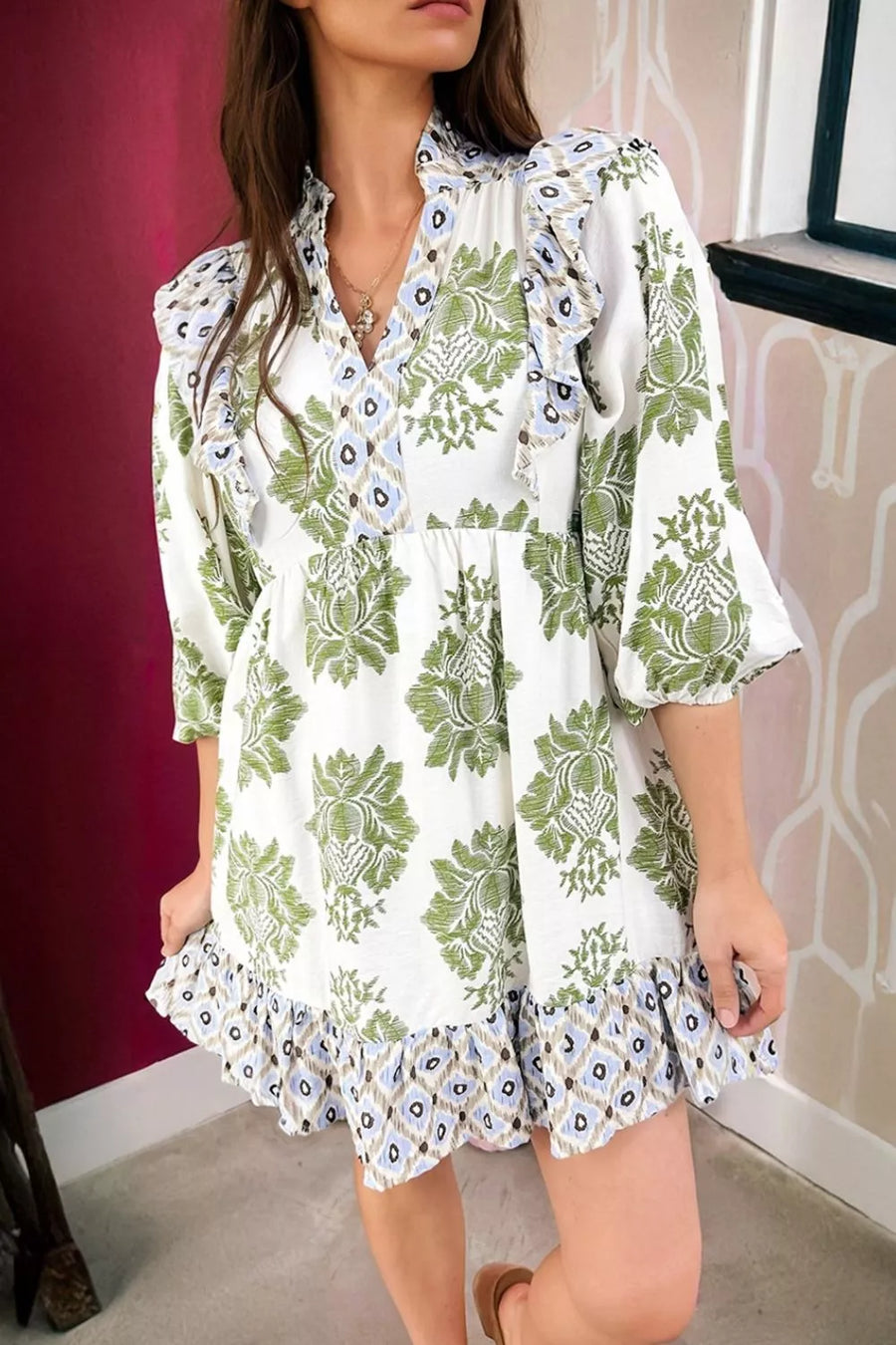 White mini dress with green floral print, ruffled neckline and hem, and patchwork detail.