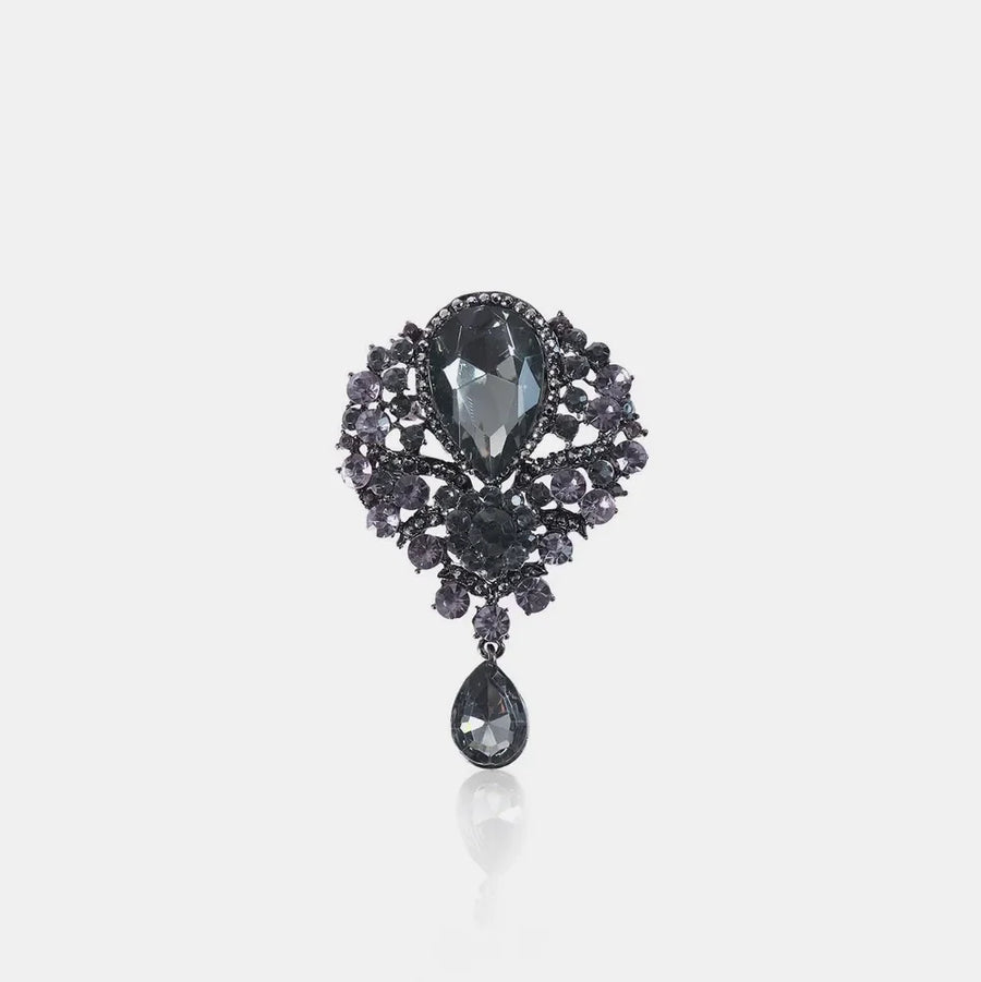 Black teardrop embellished brooch with faceted stones and dangling charm.