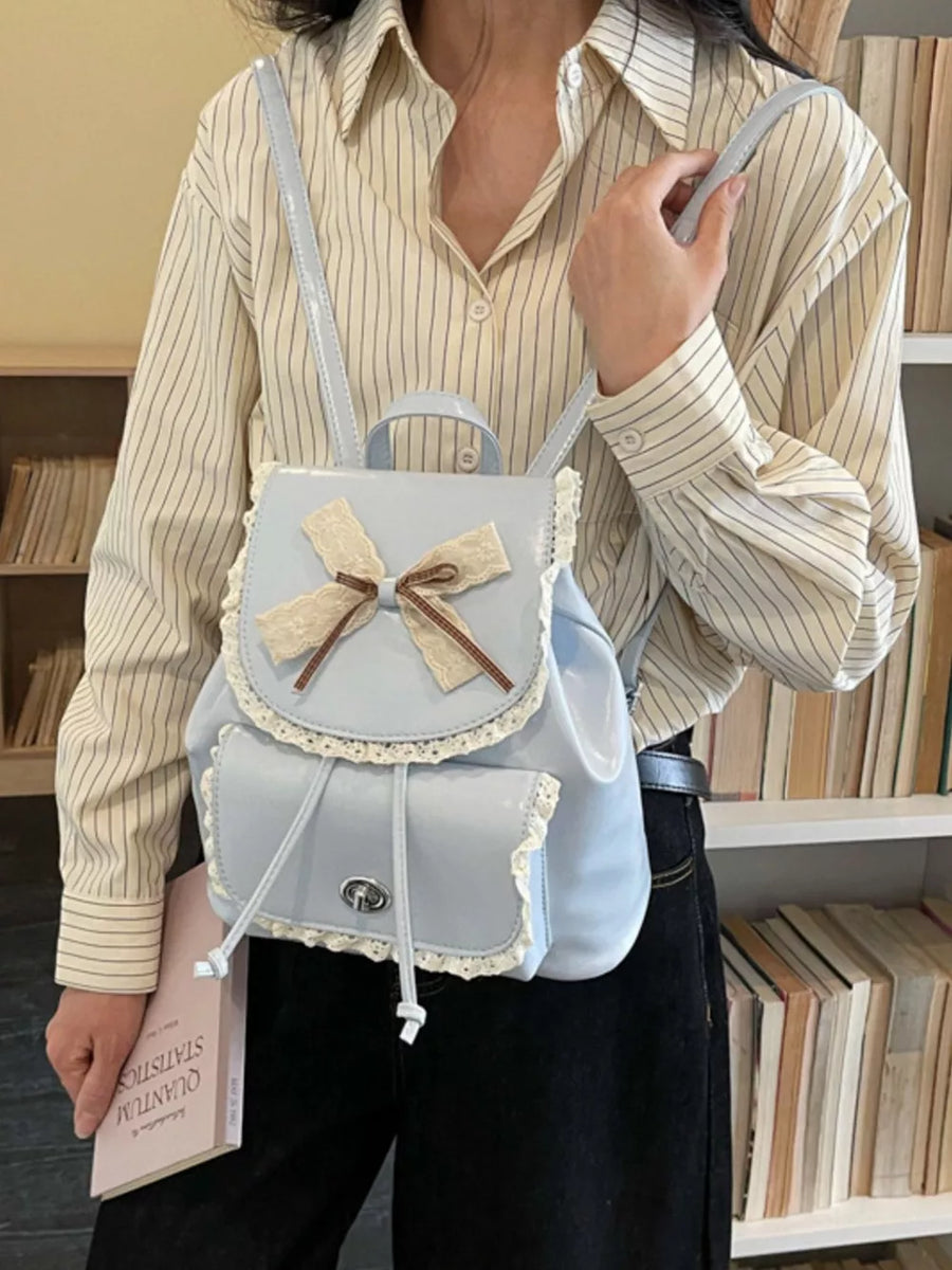 Blue mini backpack with lace trim, bow detail, and drawstring closure.