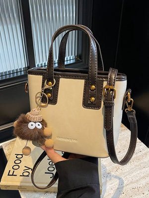 Mini leather crossbody bag in beige with brown trim and a fuzzy charm.
