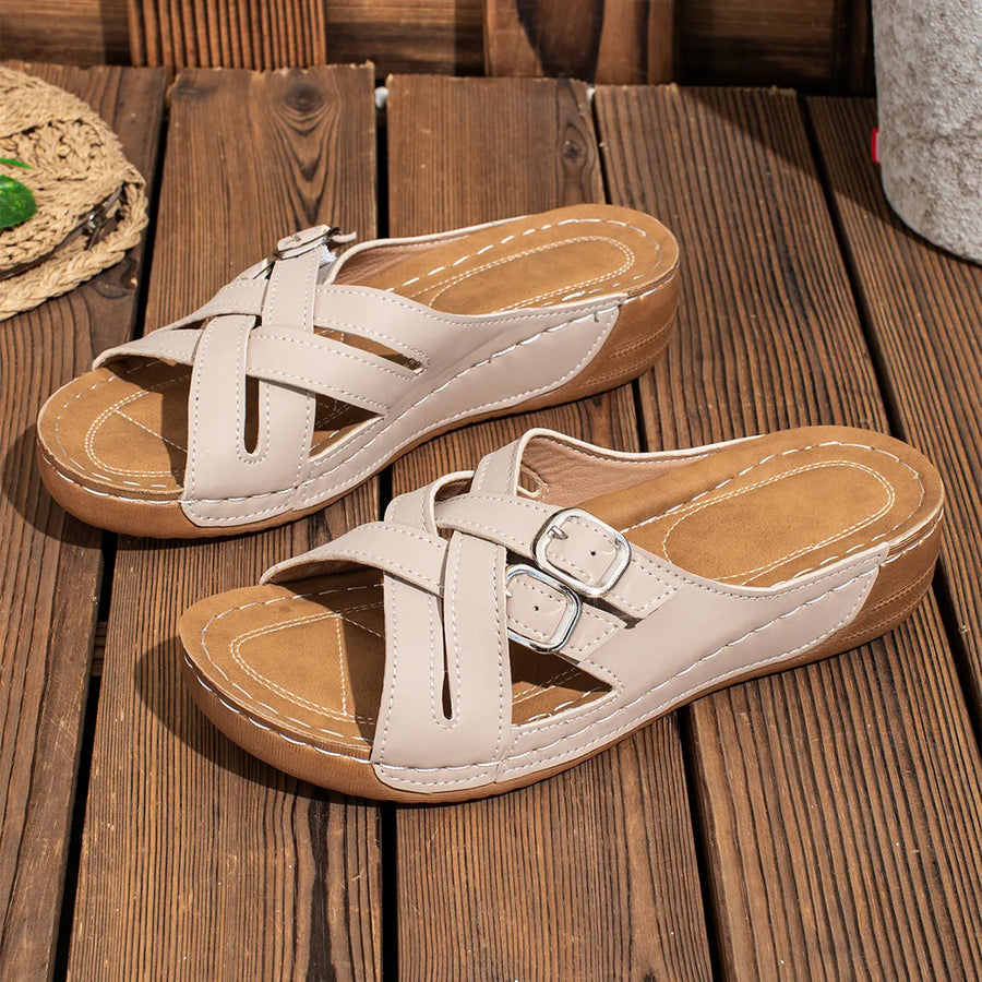 Beige crisscross buckle detail slides with a contoured footbed and wedge sole.