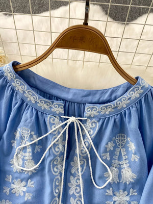 Blue embroidered tie-neck blouse with balloon sleeves and intricate floral details.