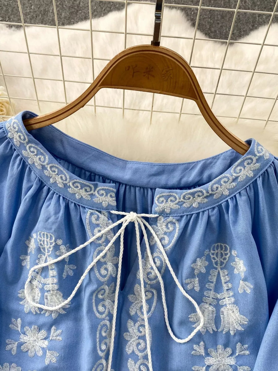 Blue embroidered tie-neck blouse with balloon sleeves and intricate floral details.