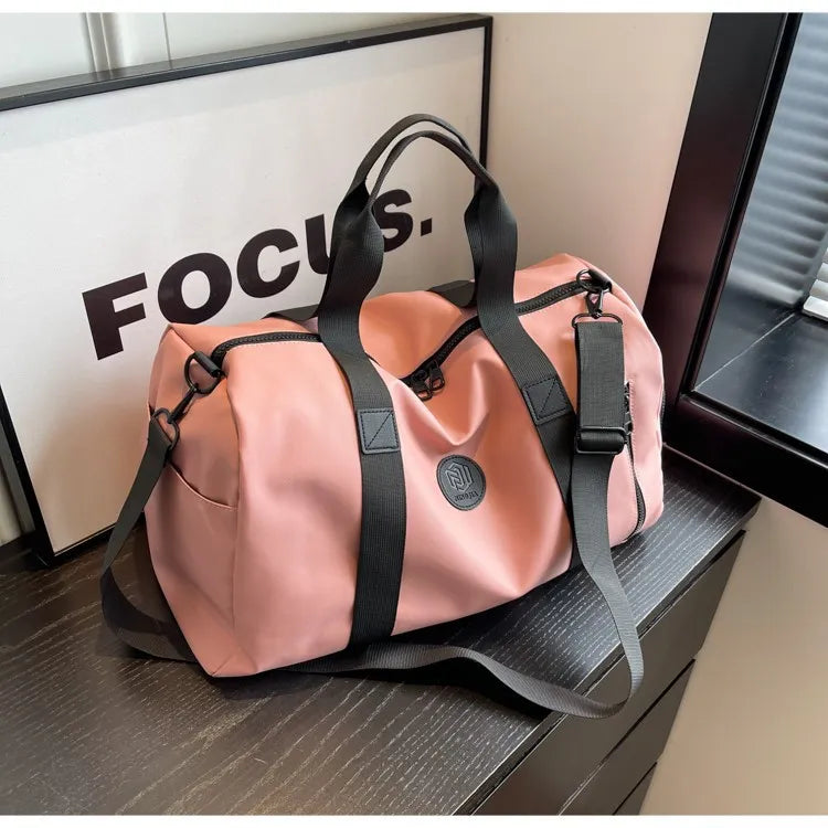 Dusty pink canvas duffel bag with black contrast straps and shoulder strap.