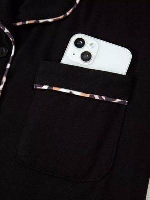 Black pajama top with leopard trim pocket and collar detail, phone shown.