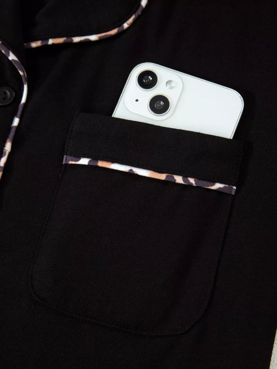 Black pajama top with leopard trim pocket and collar detail, phone shown.