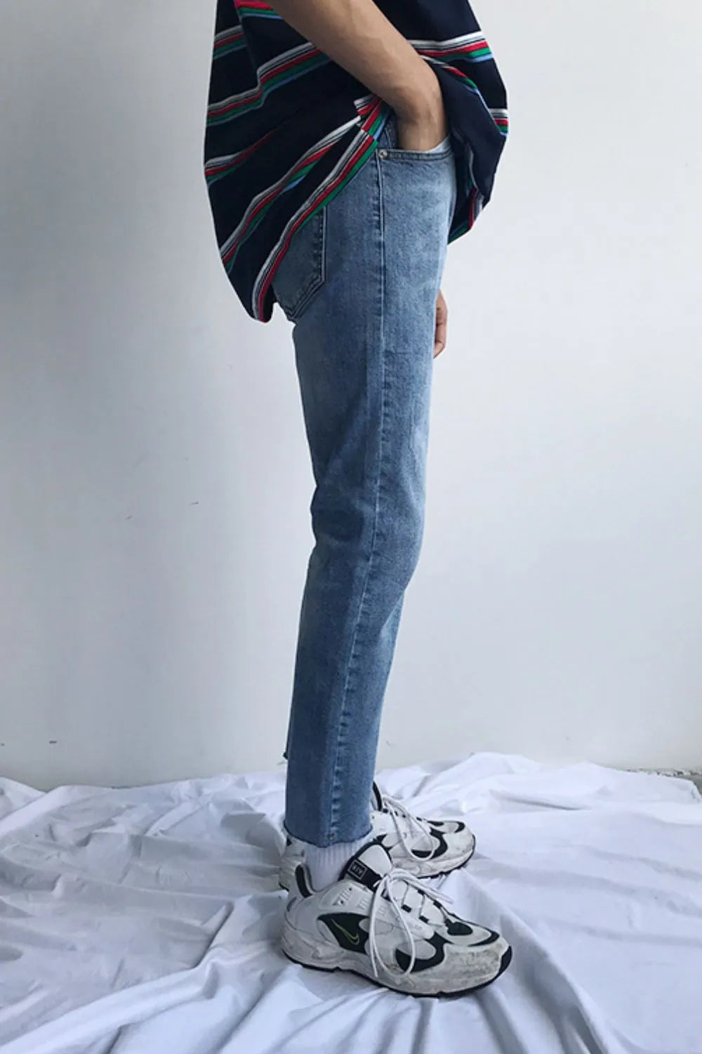 Medium wash denim jeans with raw hem and slim fit, styled with a striped shirt and sneakers.