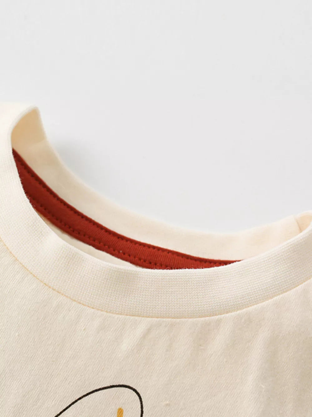Cream cotton t-shirt with cartoon animal graphic and red trim neckline.