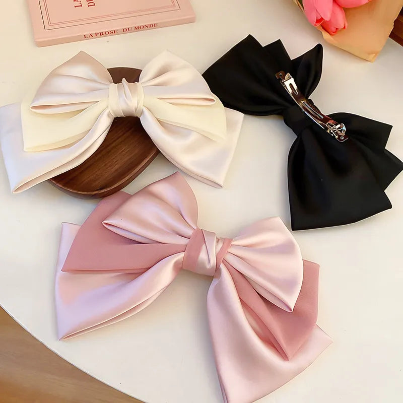 Satin bow barrettes in blush pink, ivory, and black with alloy clips.