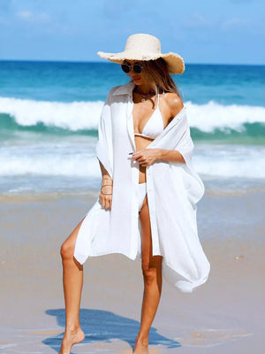 White button-up cover-up with high side slits, worn open over a bikini on the beach.