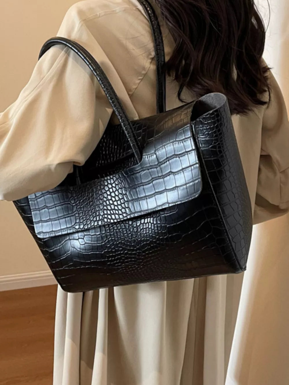 Black crocodile-embossed medium tote bag with a flap closure and top handles.