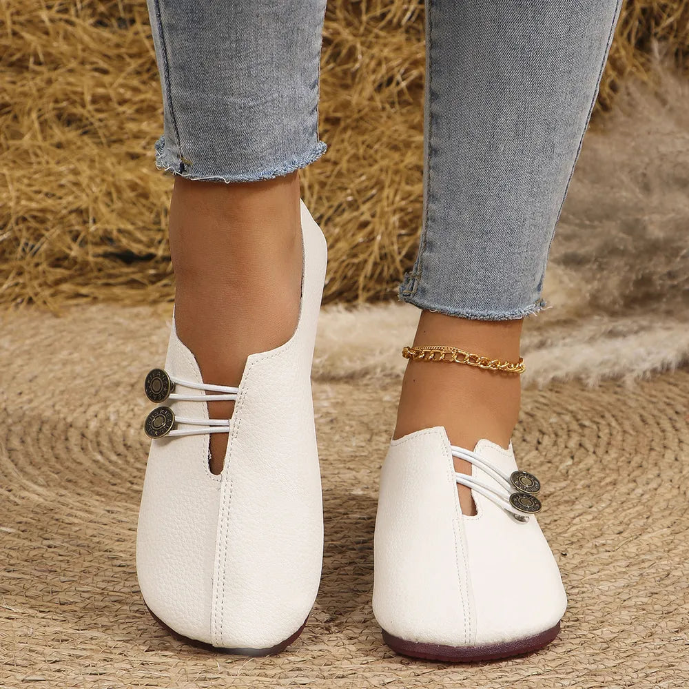 White leather slip-on flats with antique gold button detail and elastic straps.