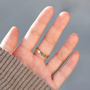 Gold-plated ring with PRAY engraved, worn on finger.