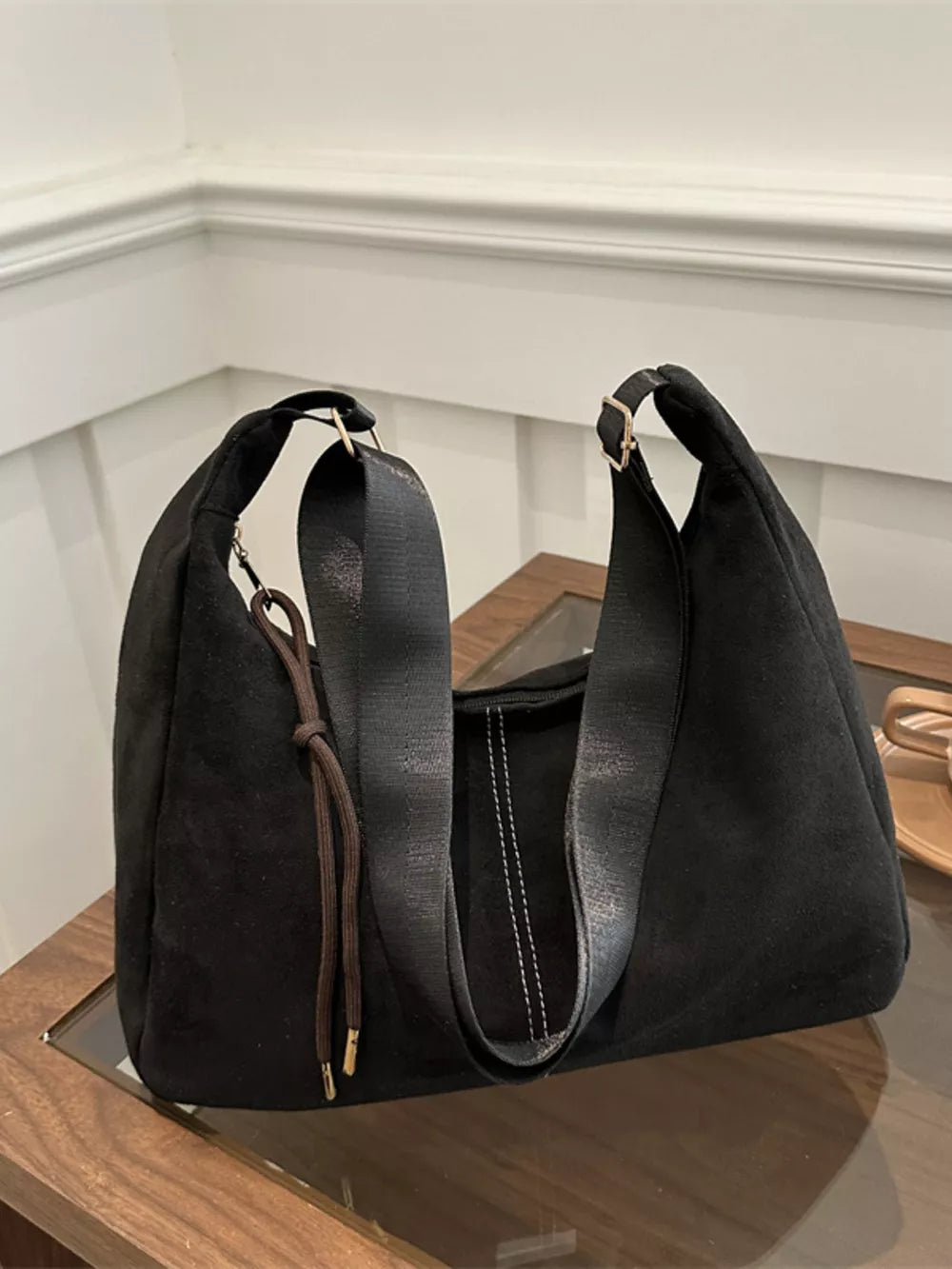 Black suede crossbody bag with adjustable strap and drawstring detail