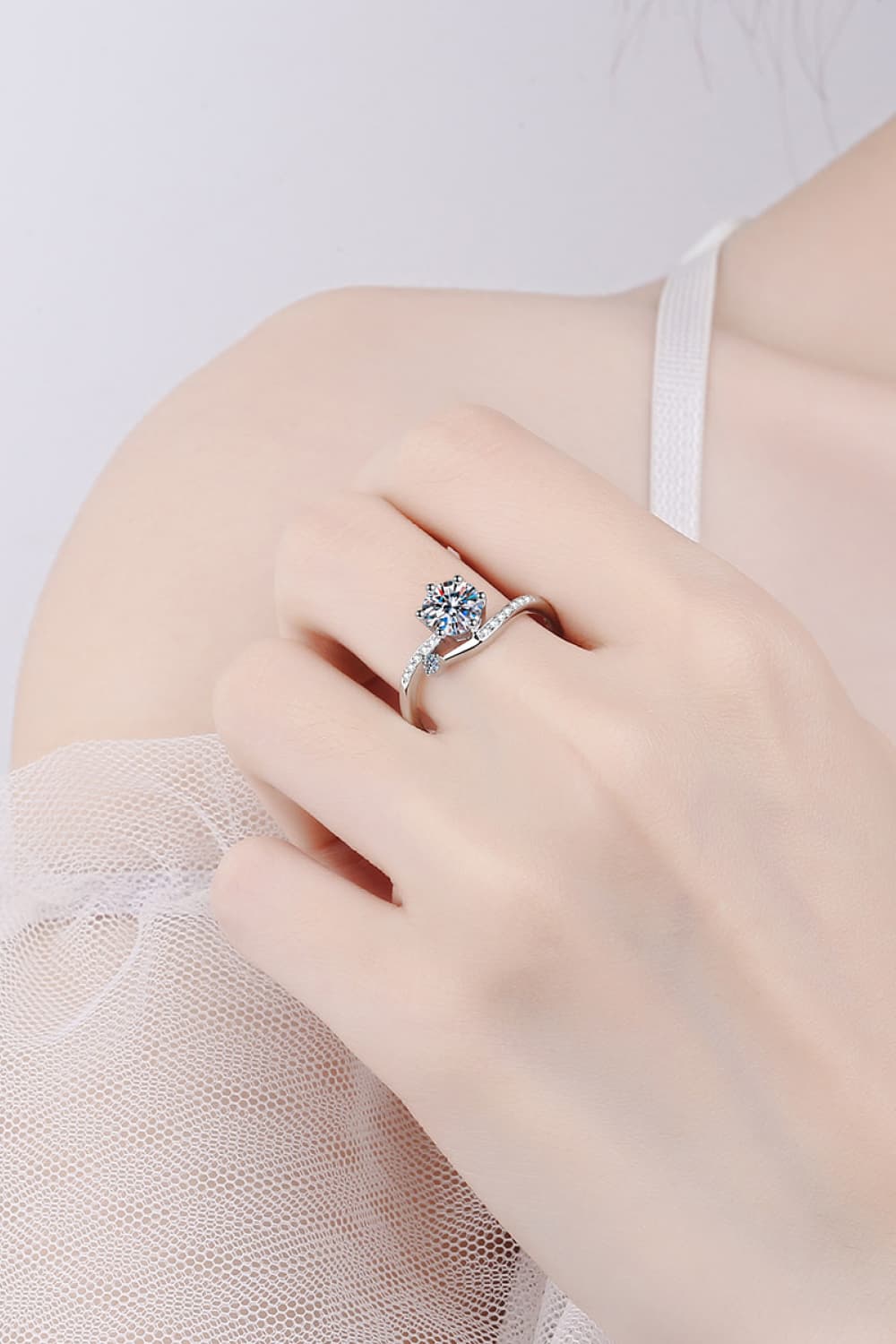 Silver moissanite bypass engagement ring with pavé band and round center stone.