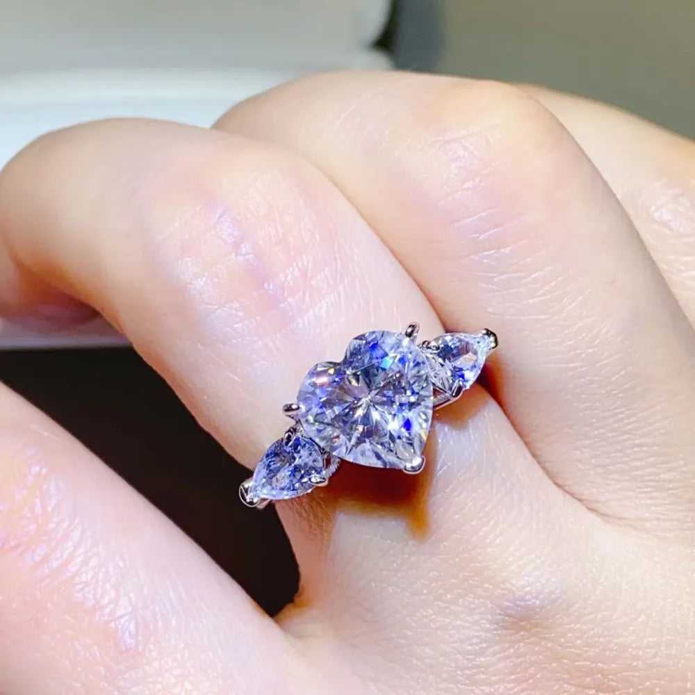 Silver heart-cut diamond trilogy ring with pear-shaped side stones on a hand.