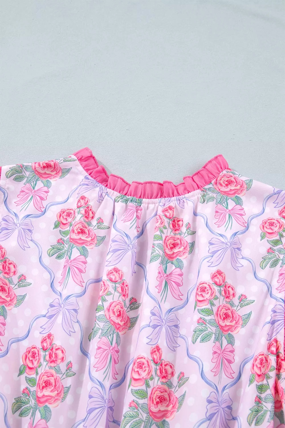 Floral tiered ruffle dress with pink roses and bows on a light pink polka dot background.