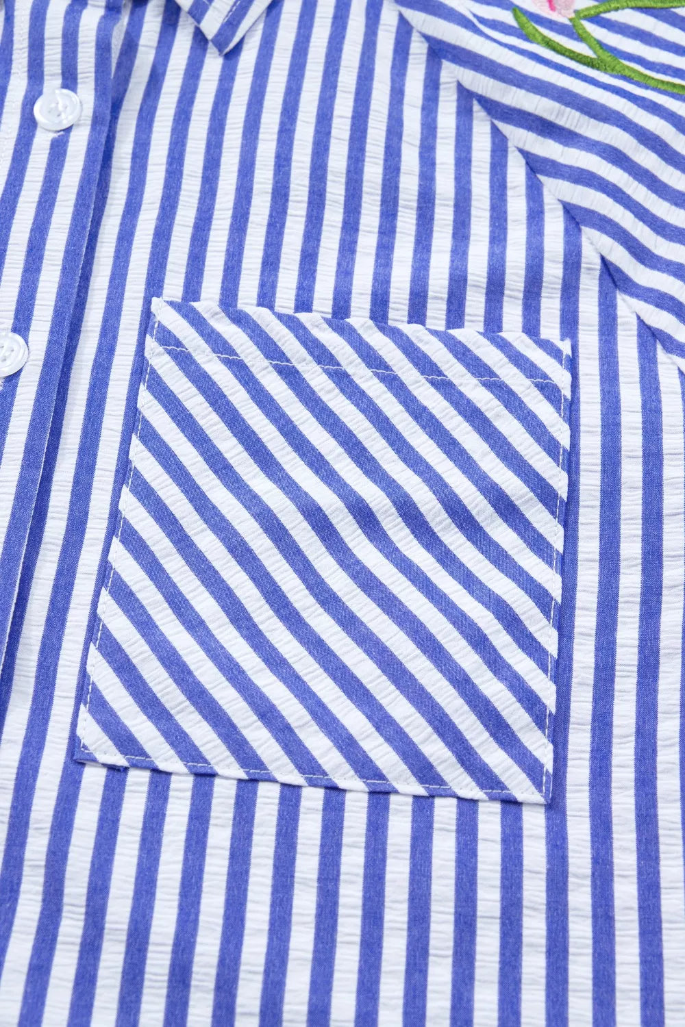 Blue and white striped button-down shirt with a pocket and floral embroidery detail.