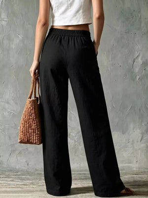 Black wide-leg linen pants with elastic waist and side pockets, styled with a white crop top and straw bag.
