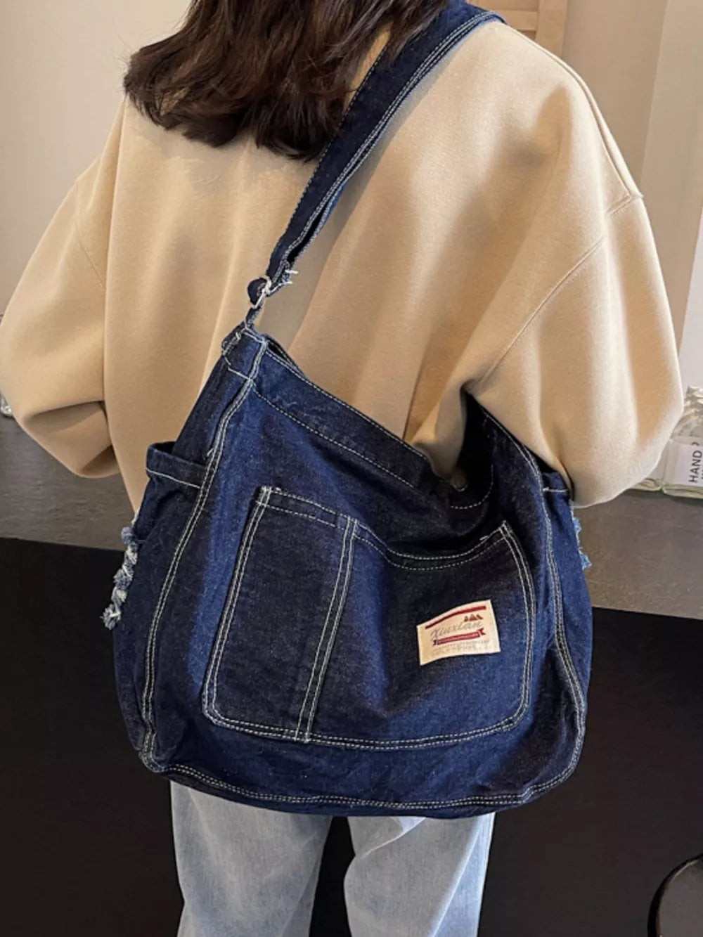 Slouchy dark blue denim crossbody bag with contrast stitching and front pockets.