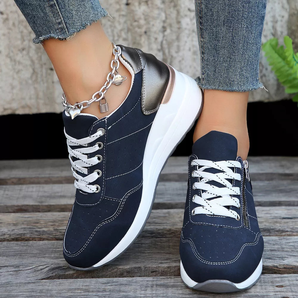 Navy lace-up wedge sneakers with white laces and a side zipper, featuring a metallic heel detail and charm anklet.
