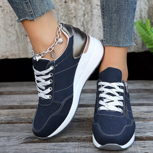 Navy lace-up wedge sneakers with white laces and a side zipper, featuring a metallic heel detail and charm anklet.