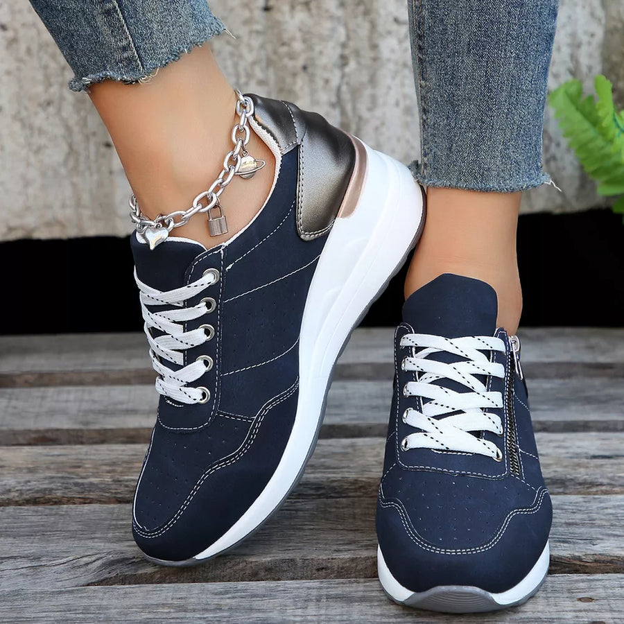 Navy lace-up wedge sneakers with white laces and a side zipper, featuring a metallic heel detail and charm anklet.