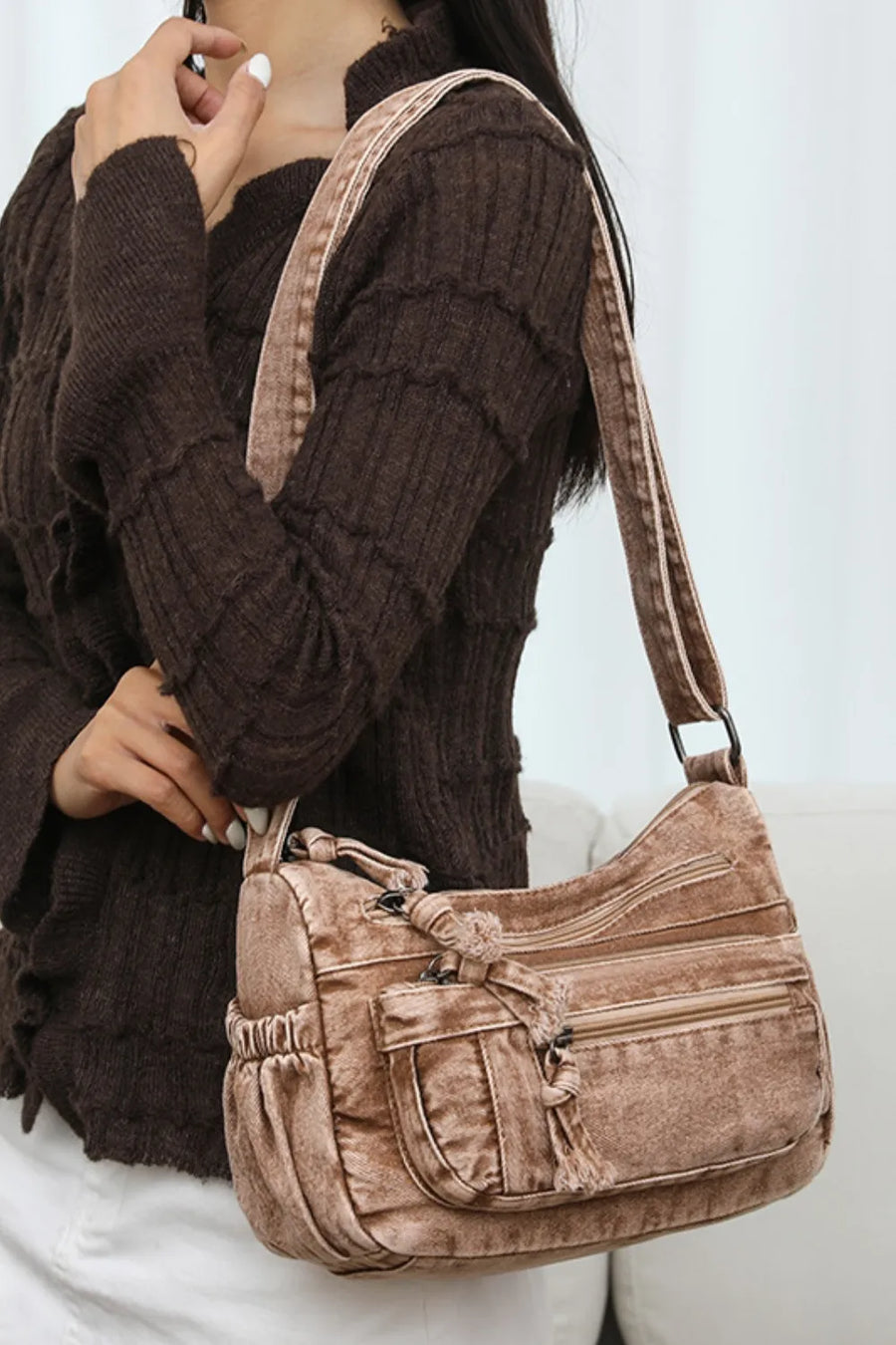 Acid wash denim crossbody bag in camel with multiple zippered pockets and tassel detail.