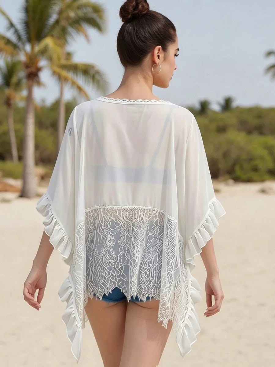White sheer flowing cover-up with lace trim and ruffled sleeves, worn over denim shorts.