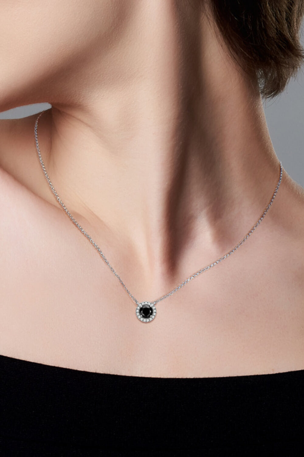Black Halo Moissanite necklace with a round black center stone and halo of white stones on a silver chain.