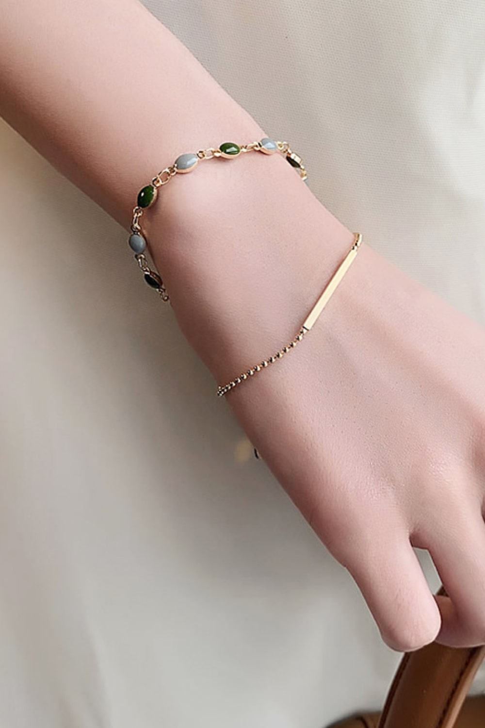 Gold dual chain bracelet with green and gray stones and a bar accent