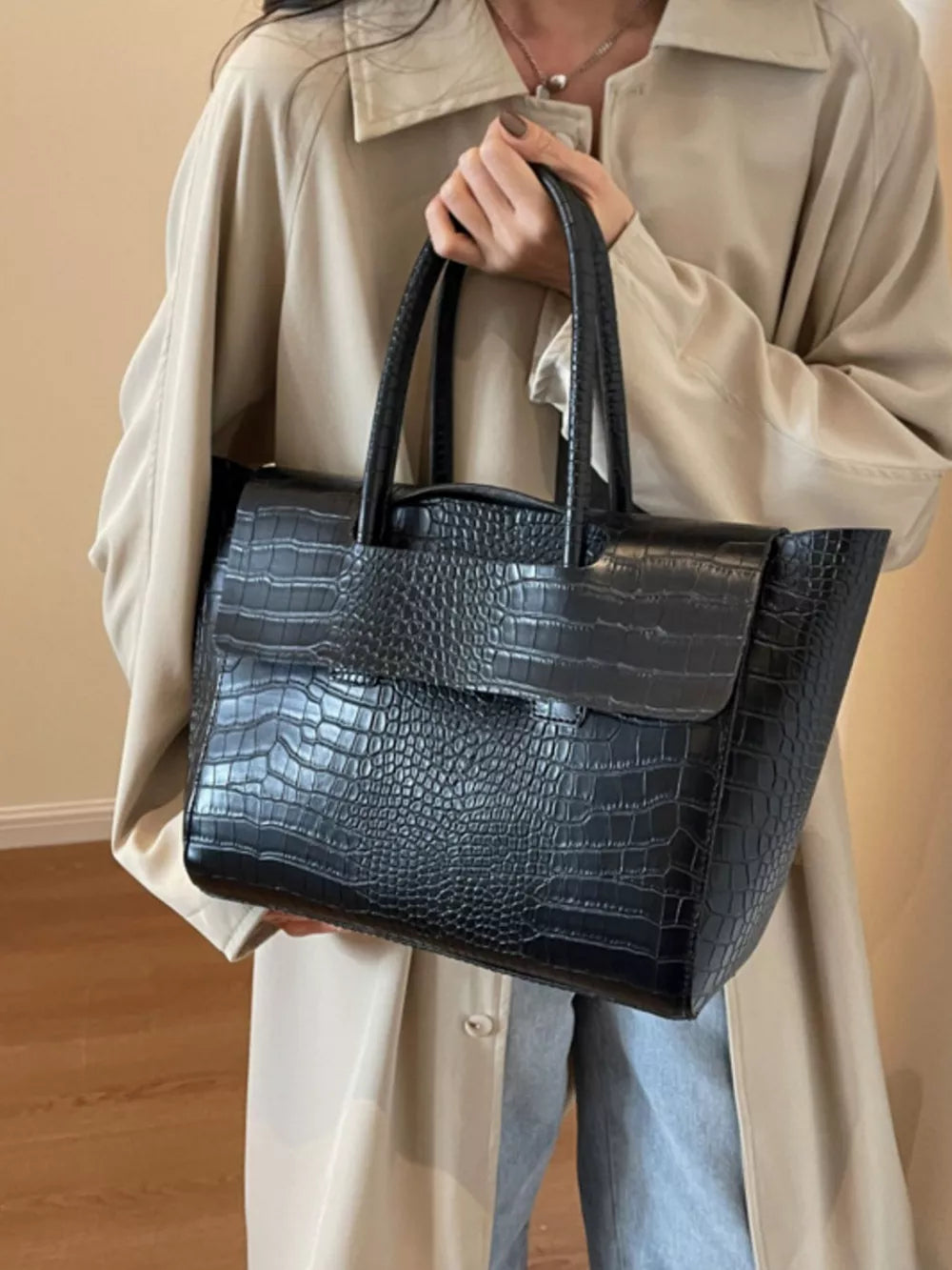 Black crocodile-embossed medium tote bag with top handles and flap closure.