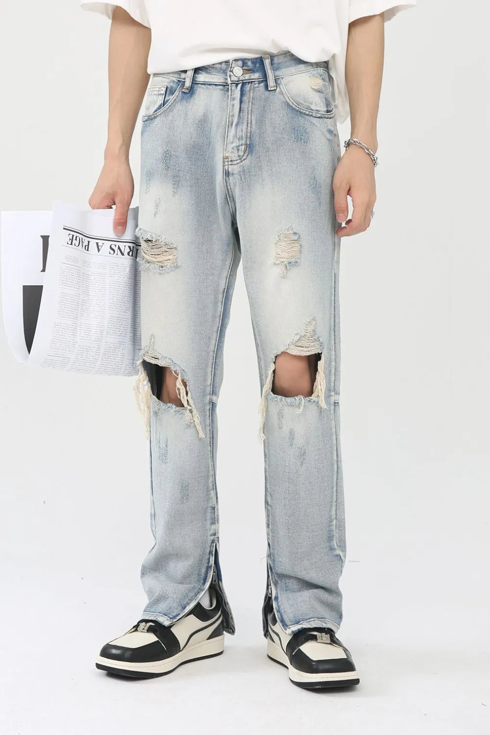 Light wash denim trousers with distressed knee slits and ankle zippers.