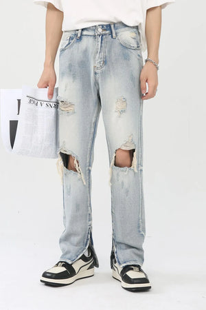 Light wash denim trousers with distressed knee slits and ankle zippers.
