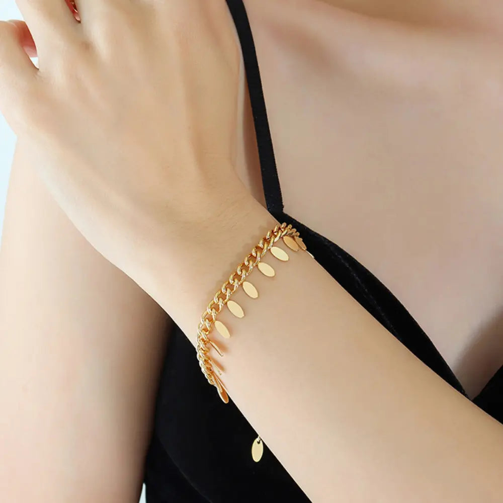 Gold oval link bracelet with dangling charms on a woman's wrist