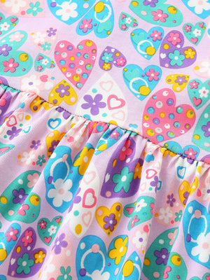 Baby dress with a lilac background and a colorful heart and flower print, featuring a ruffled hem.