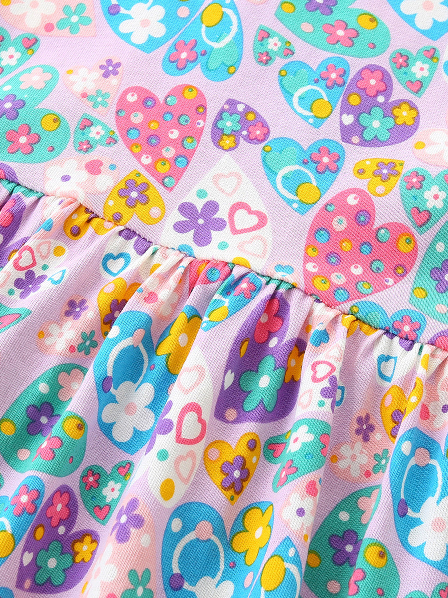 Baby dress with a lilac background and a colorful heart and flower print, featuring a ruffled hem.