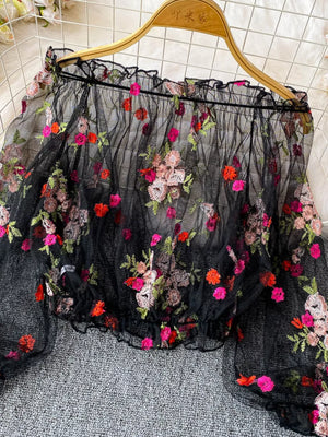 Black off-shoulder t-shirt with colorful floral embroidery and ruffled neckline.