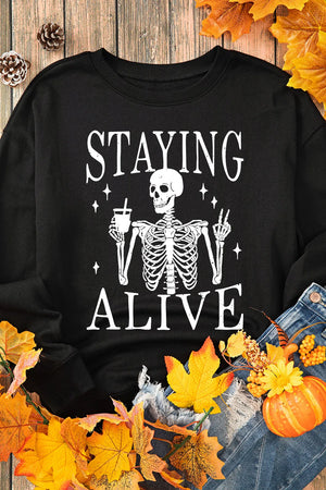 Black graphic sweatshirt with skeleton saying Staying Alive, holding a drink and flashing peace sign.